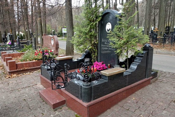 Памятник-арка из чёрного гранита в окружении туй